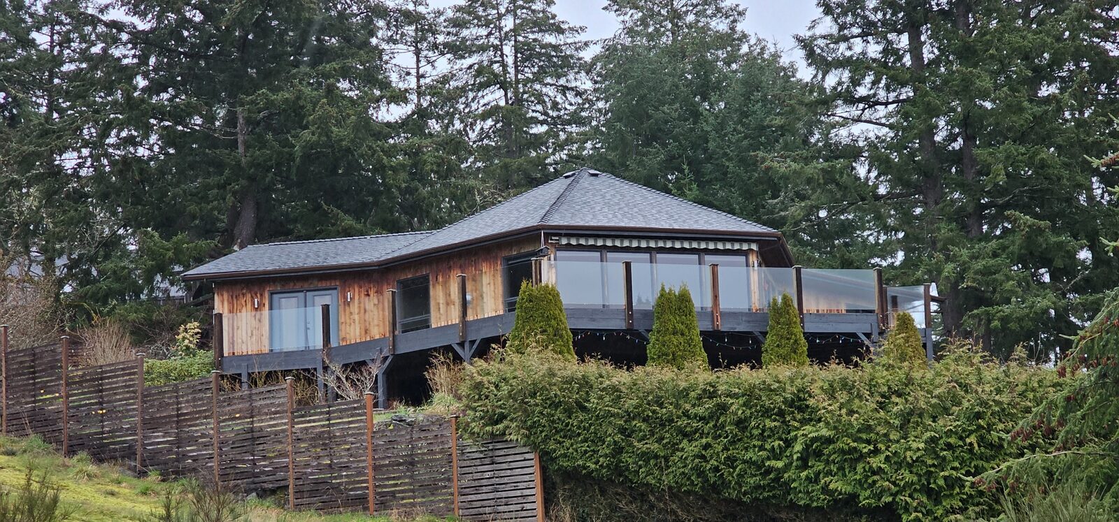Completed asphalt shingle reroof — island property with cedar siding, glass deck rail, and water views